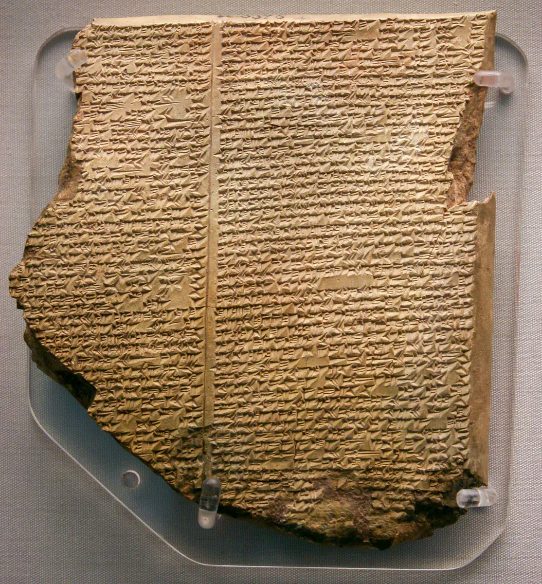 Fotografía del original: Tablilla del Diluvio, XI de la epopeya de Gilgamesh. Fotografía nítida de la tablilla completa conservada, con dos columnas y borde fragmentado; soportes de vitrina visibles.