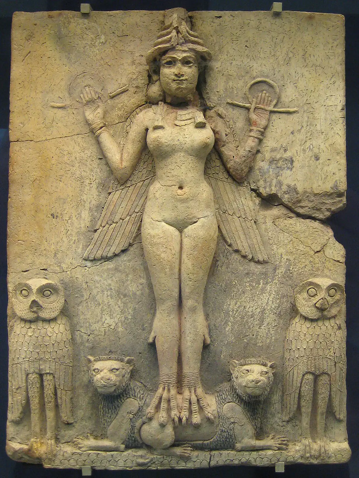 Fotografía del original: Relieve Burney o Reina de la Noche. Relieve completo, figura alada, dos búhos y dos leones visibles. Iluminación de vitrina, soportes visibles.