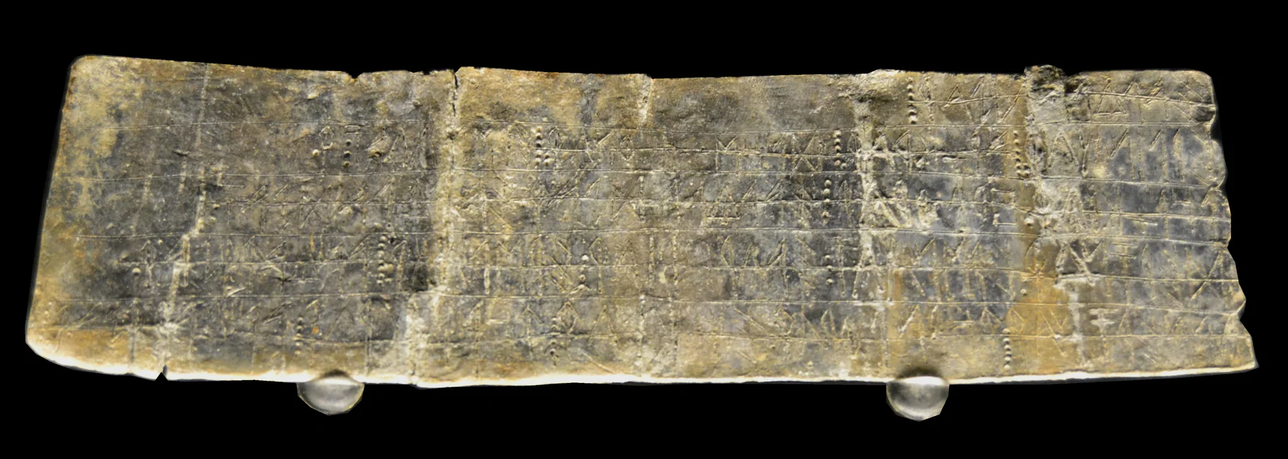 Plomo I de La Bastida de les Alcusses: fotografía del original recortada sobre negro, con dos soportes transparentes conservados; signos incisos sin redibujado.