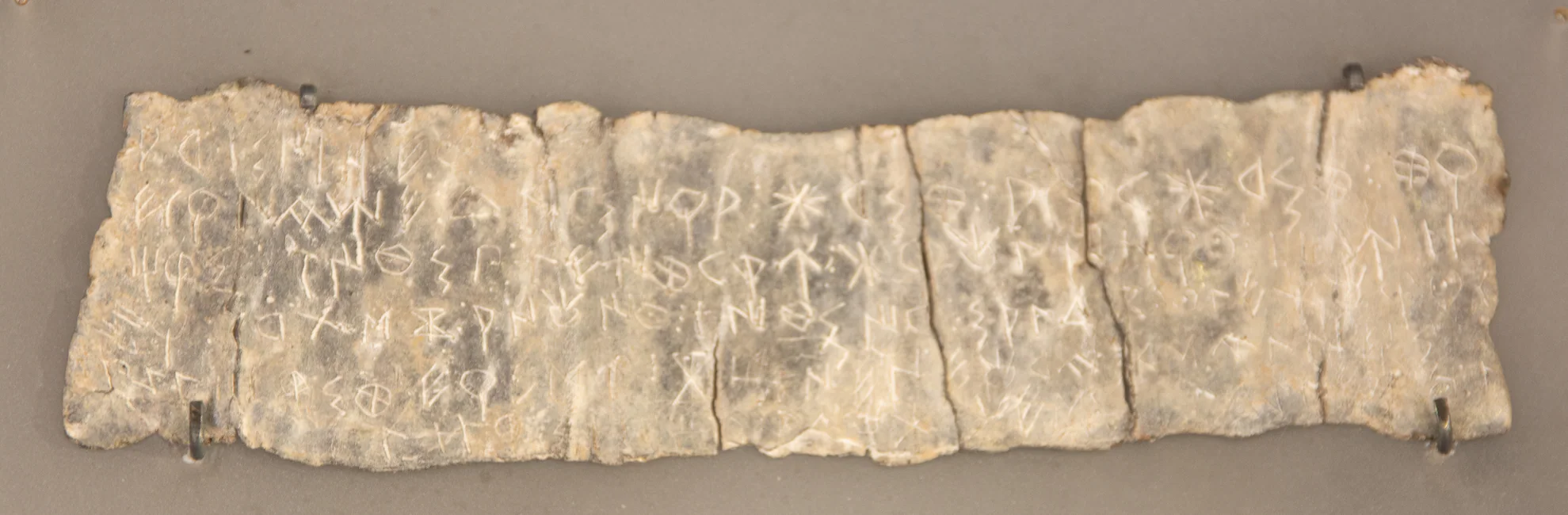 Lámina de plomo MAC ULL-03309 de Ullastret: recorte de la fotografía del original, con fondo gris y grapas de museo conservados; signos incisos sin redibujado.