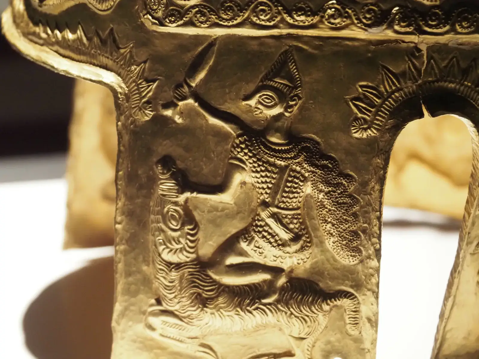 Detalle de una carrillera del casco de Coțofenești: guerrero arrodillado con un carnero en una escena de sacrificio.